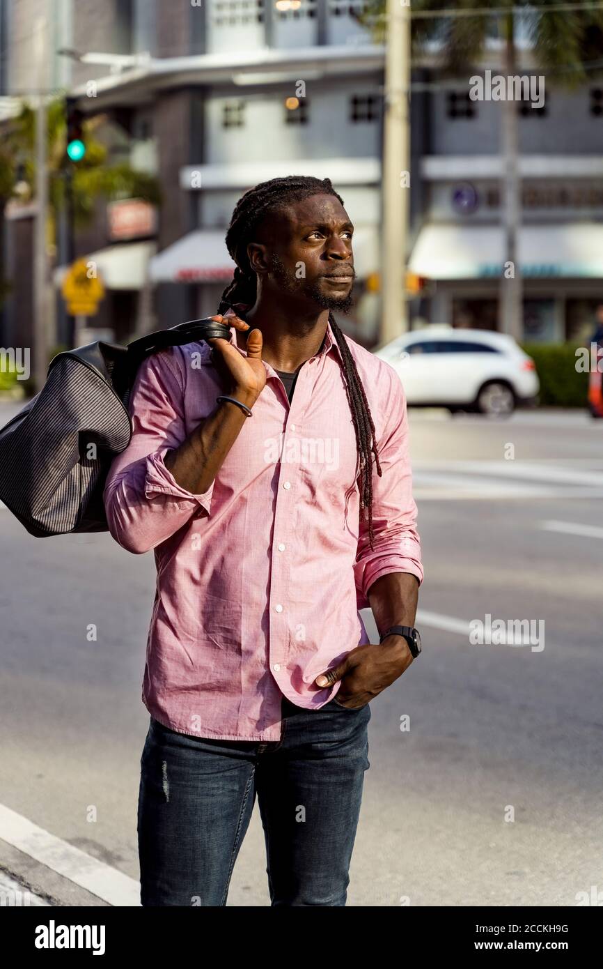 Nachdenklicher afro junger Mann mit Tasche auf der Straße in Miami, Florida, USA Stockfoto