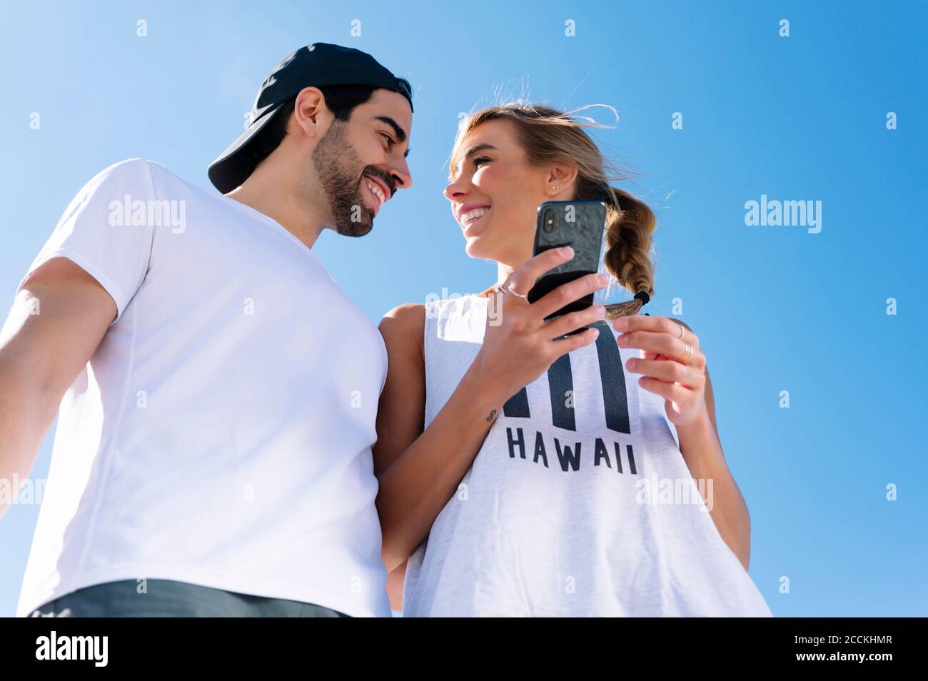 Lächelnde Frau hält Smartphone Blick auf Freund gegen klar Blauer Himmel Stockfoto