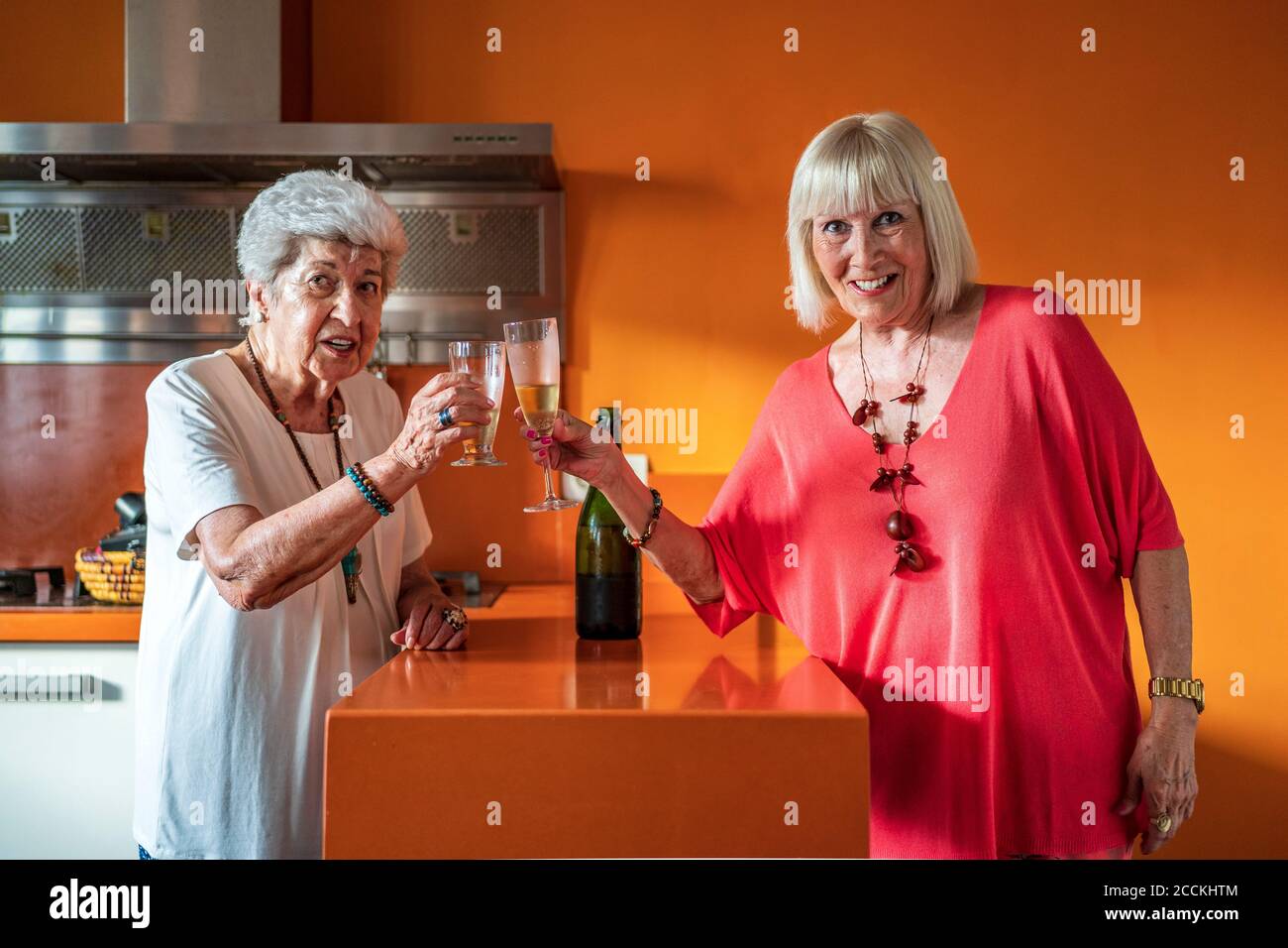 Lächelnde ältere Freundinnen, die Champagner-Flöten toasten, während sie anstanden Zu Hause Stockfoto
