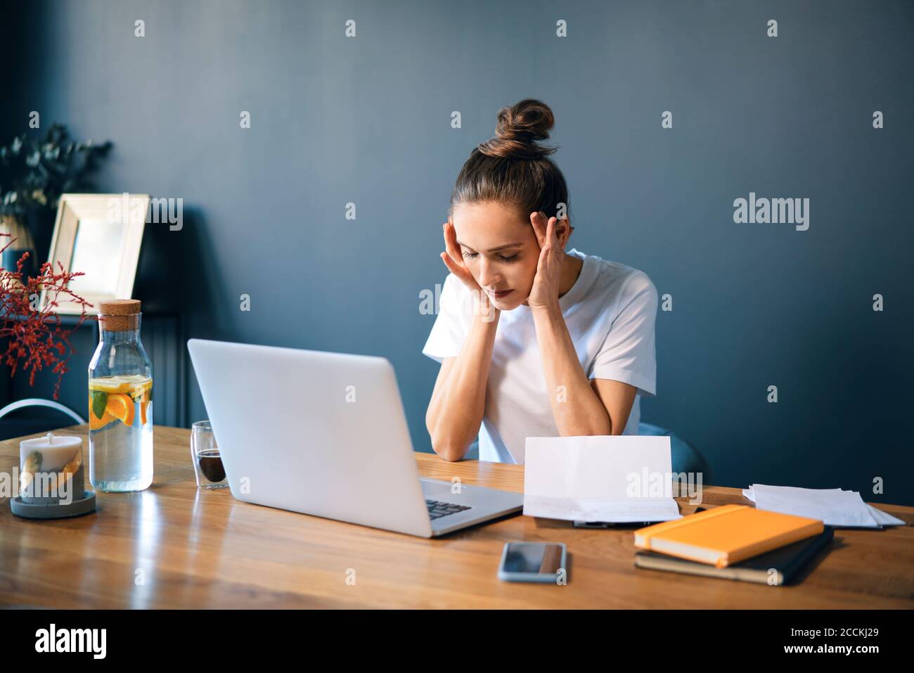 Weibliche Unternehmerin mit Kopf in den Händen sitzen am Schreibtisch gegen Wand Stockfoto