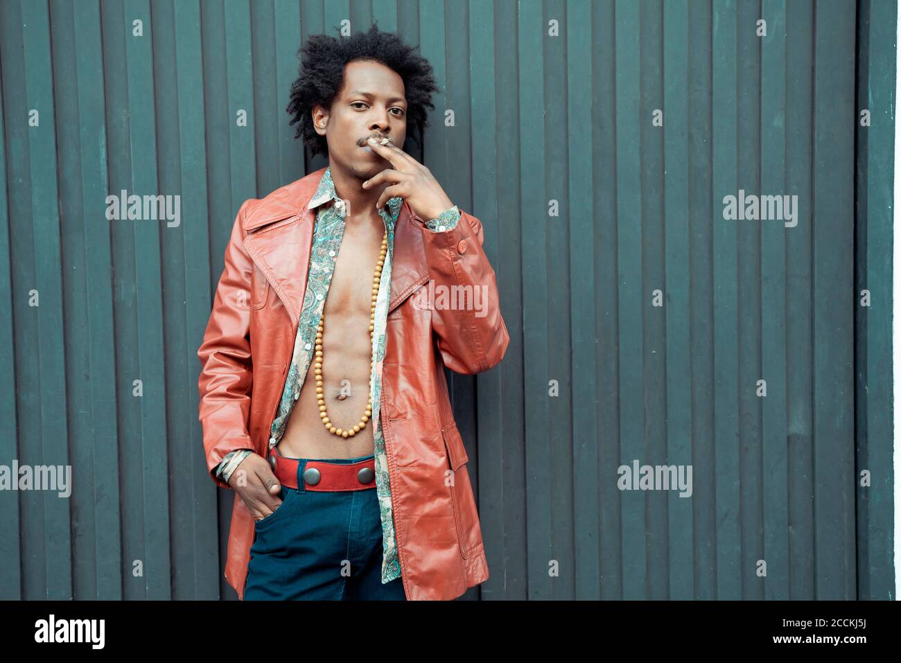 Selbstbewusster Mann in Retro-Jacke rauchen, während sie gegen schwarz stehen Wand Stockfoto