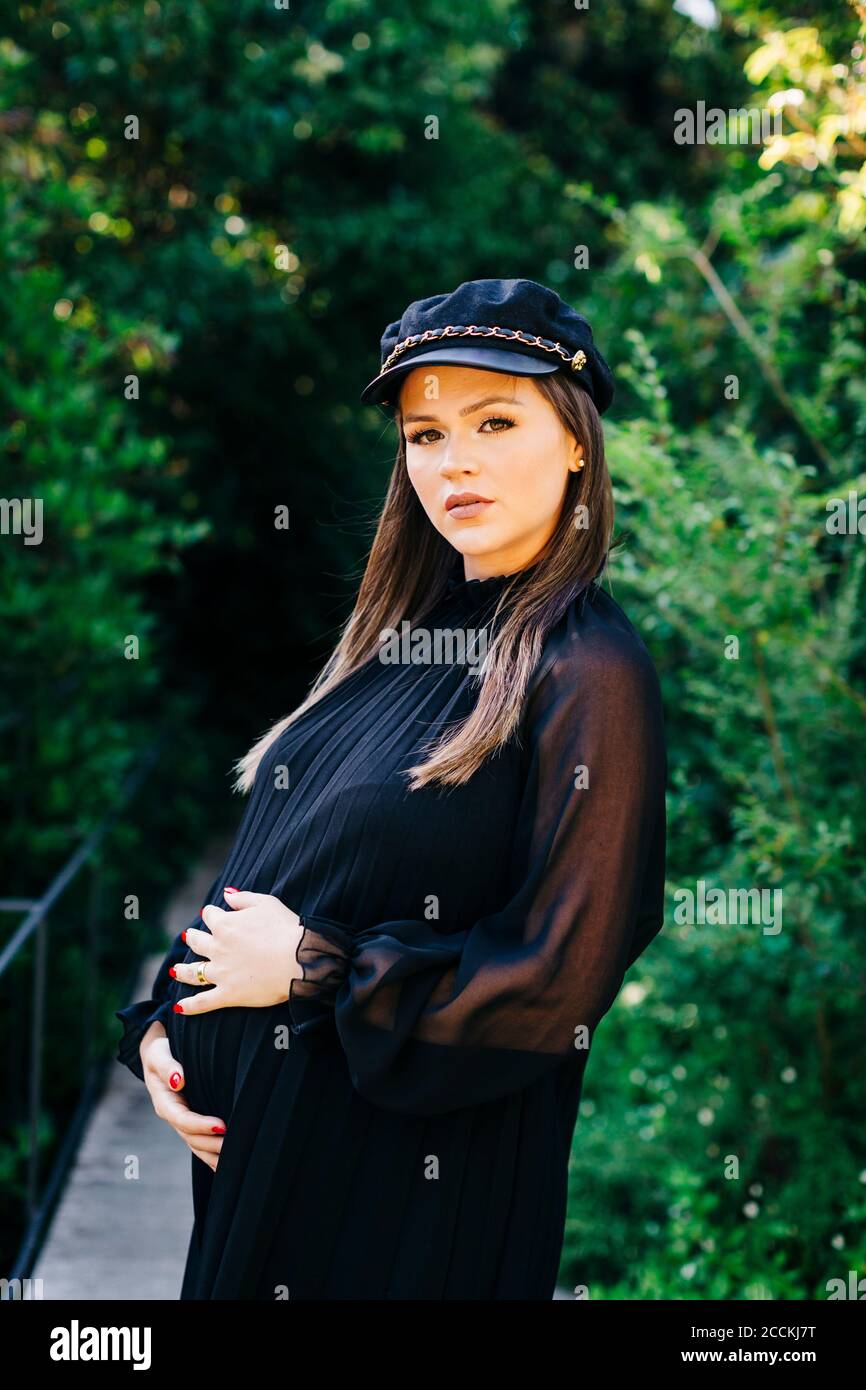 Schöne schwangere Frau, die mit Händen auf dem Bauch im Park steht Stockfoto