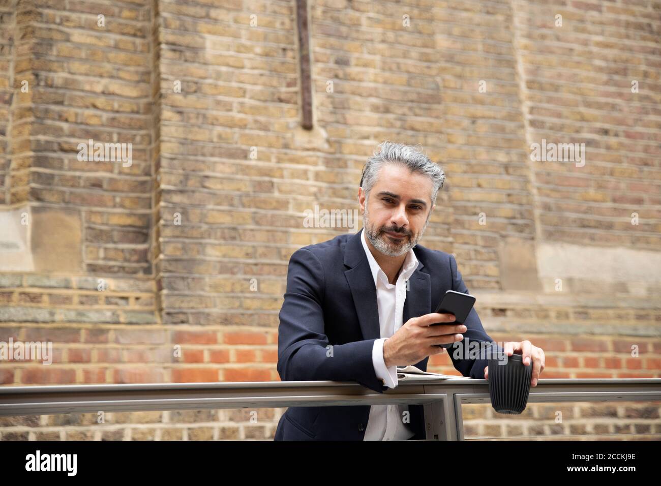 Selbstbewusster Geschäftsmann mit Smartphone gegen die Wand Stockfoto