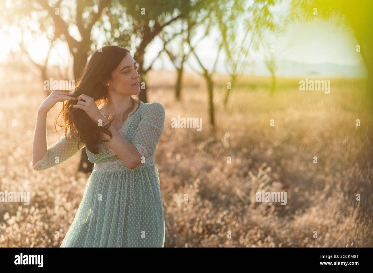 Junge Frau mit Händen im Haar auf dem Bauernhof während stehen Sonnenuntergang Stockfoto