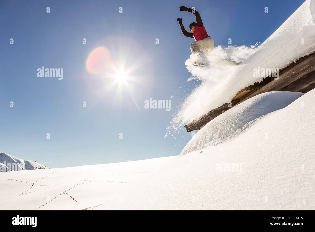 Mann, der vom Dach einer Hütte in die Tiefe springt Schnee Stockfoto