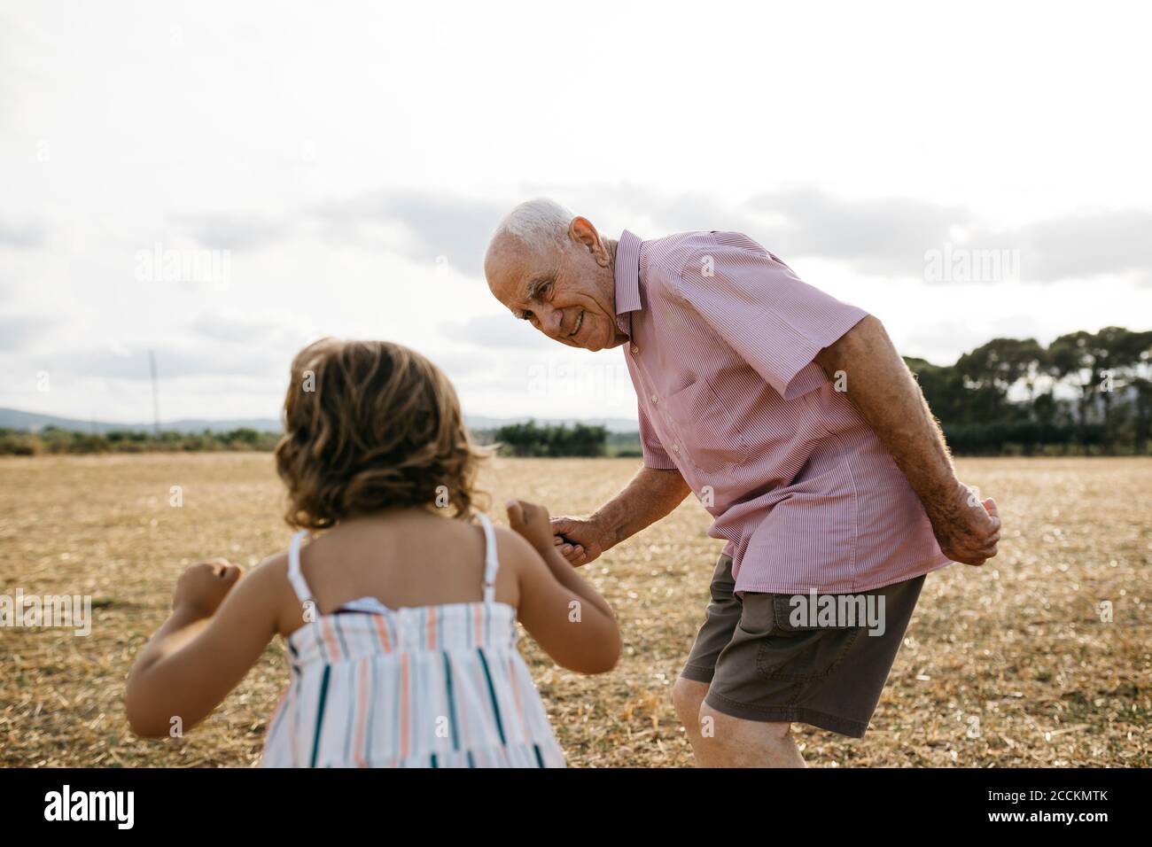 Großvater schaut Enkelin an, während er auf dem Land gegen den Himmel steht Stockfoto