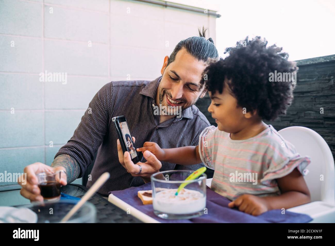 Lächelnder Vater, der der kleinen Tochter beim Essen ein Smartphone zeigt Tabelle Stockfoto