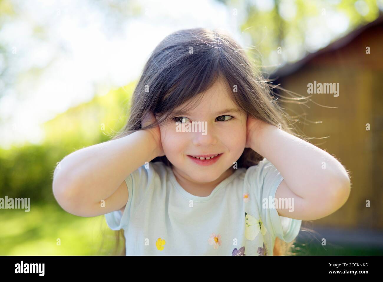 Nettes Mädchen, das Ohren auf dem Hof während des sonnigen Tages bedeckt Stockfoto