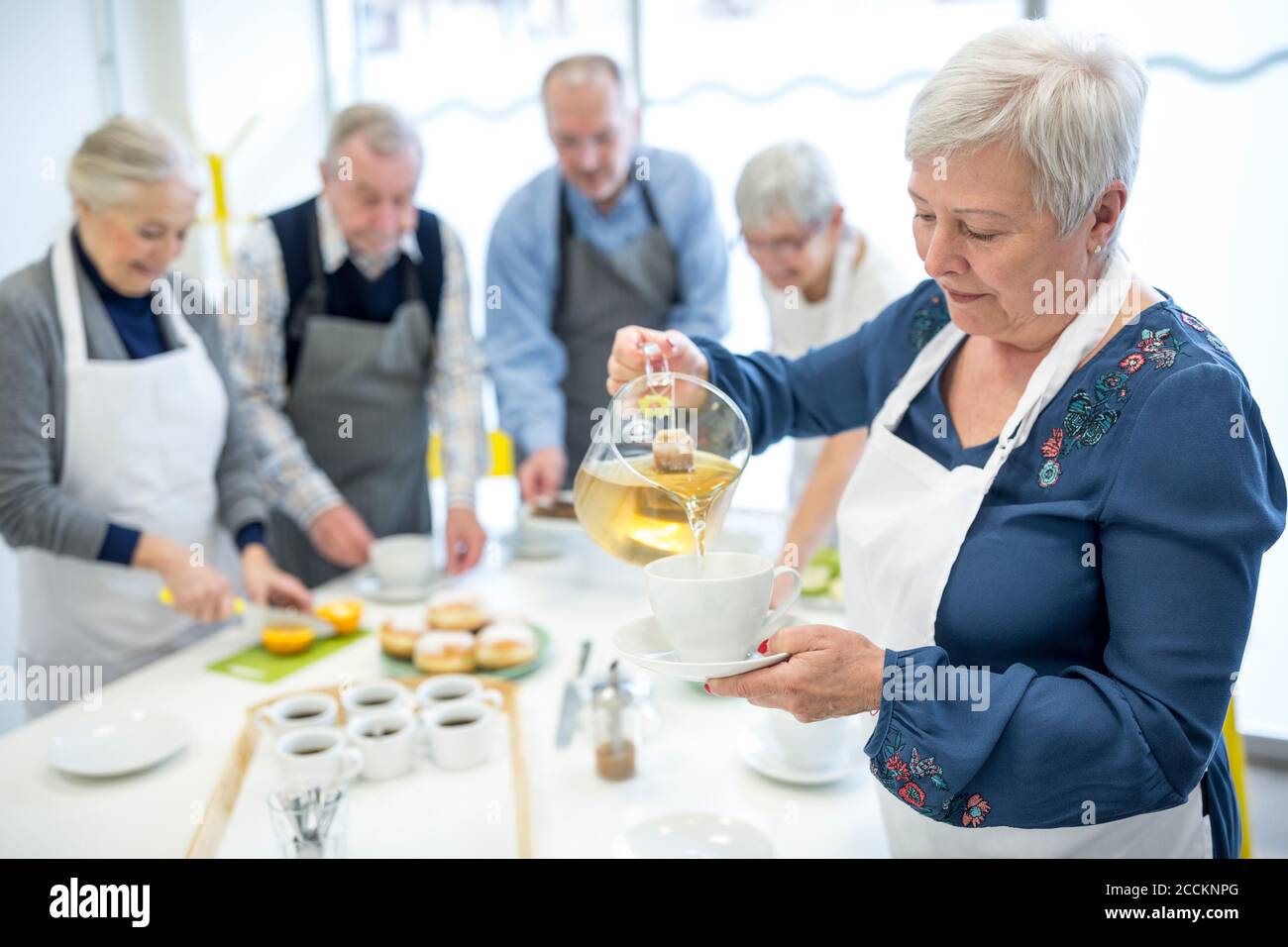 Ältere Frau gießt Tee in der Tasse für Kaffee Party in Altersheim Stockfoto
