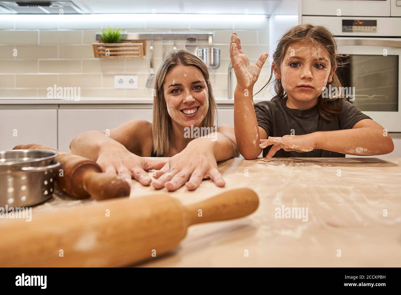 Verspielte Mutter und Tochter mit unordentlichen Gesichtern am Tisch sitzen In der Küche Stockfoto