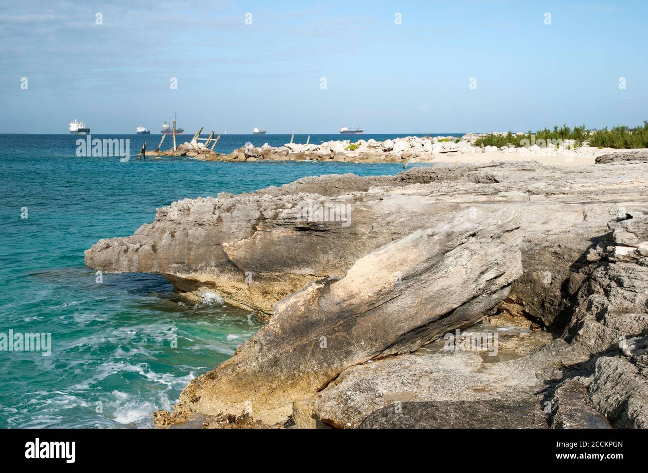 Der Blick auf Grand Bahama Island erodierte felsige Küste mit Frachtschiffen im Hintergrund (Freeport, Bahamas). Stockfoto
