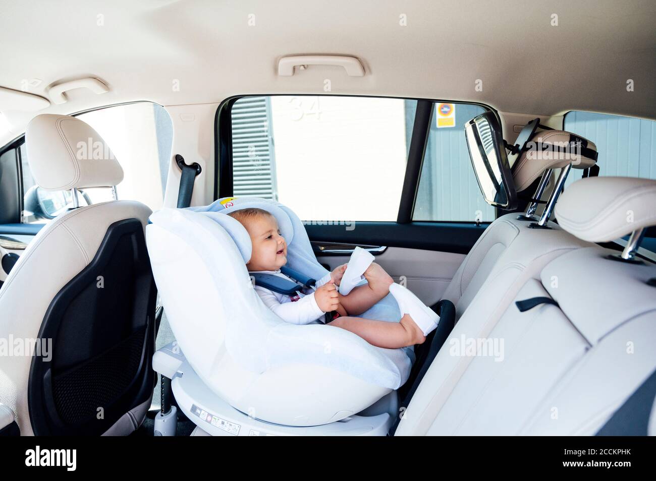 Kleiner Junge, der auf dem Kindersitz sitzt und in den Spiegel schaut In einem Auto Stockfoto