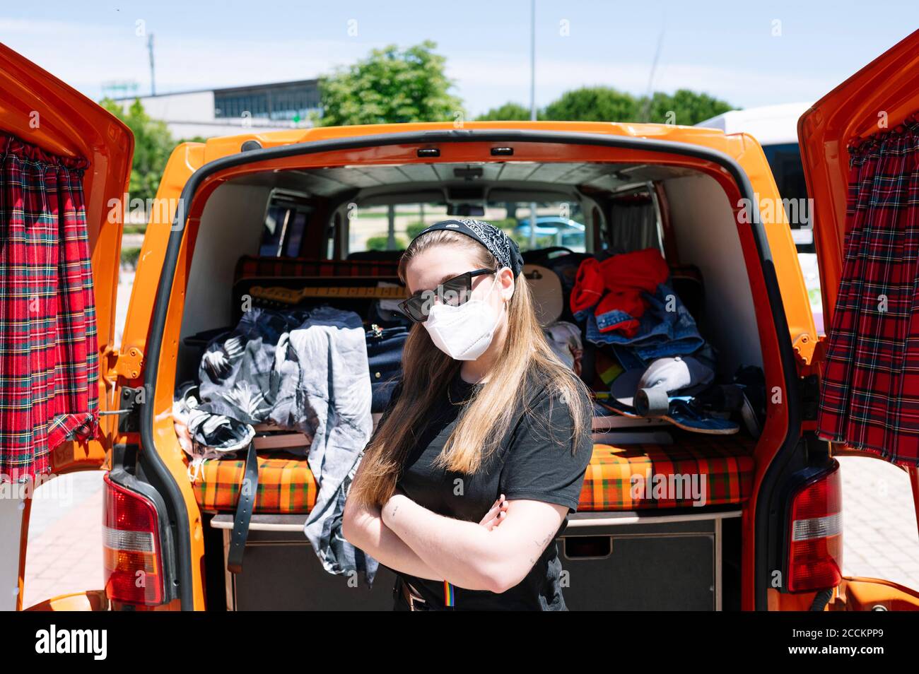 Frau mit Gesichtsmaske und Sonnenbrille stehen vor Offener Van mit gekreuzten Armen Stockfoto
