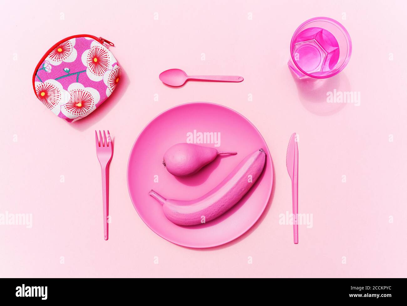 Studio Schuss von rosa Kunststoff Geschirr, Glas Wasser, rosa Früchte und kleine Tasche mit Blumenmuster Stockfoto