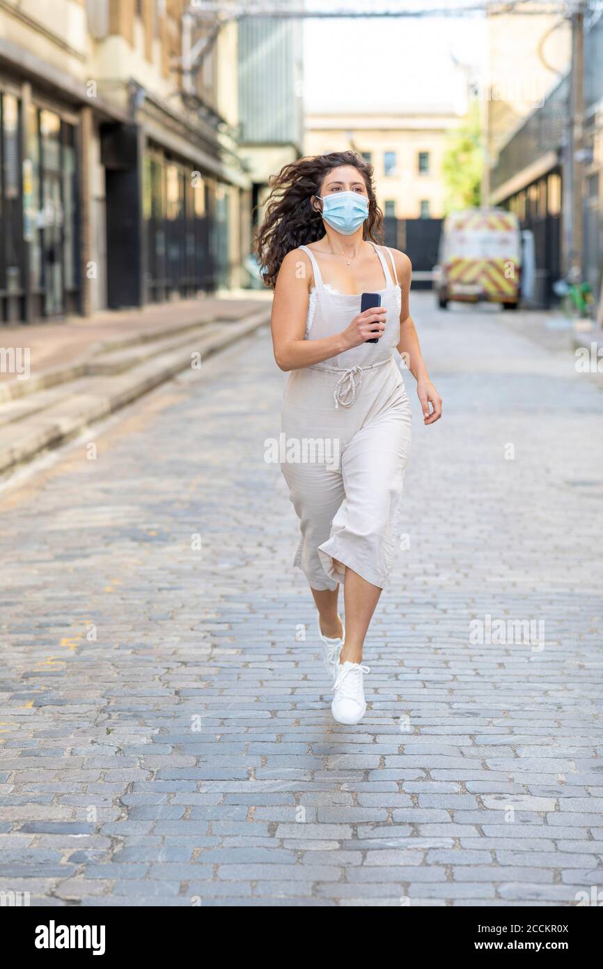 Junge Frau trägt Maske läuft auf der Straße in der Stadt Stockfoto