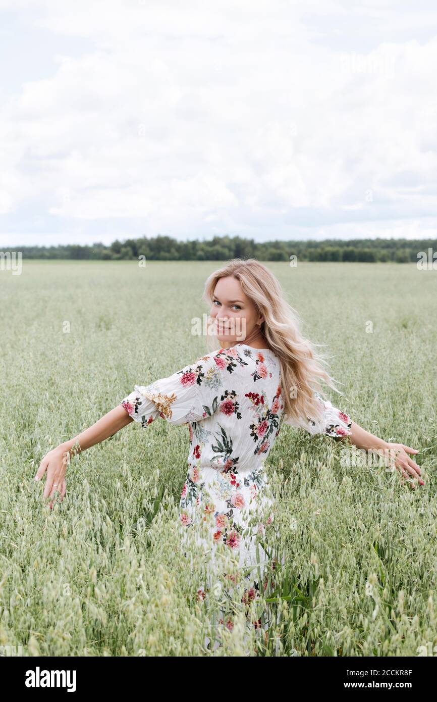 Schöne Frau mit blonden Haaren stehend inmitten Hafer Feld gegen wolkiger Himmel Stockfoto