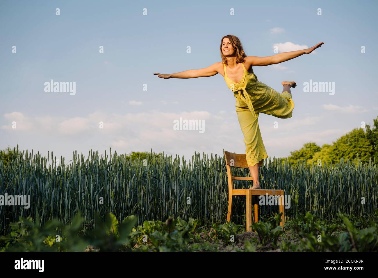 Junge Frau, die auf einem Stuhl auf dem Land vorgibt Zum Fliegen Stockfoto