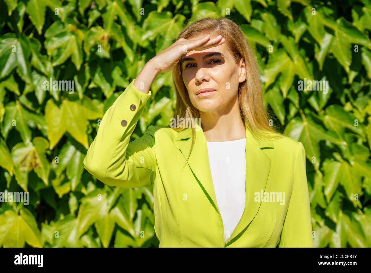 Geschäftsfrau, die die Augen abschirmt, während sie an sonnigen Tagen gegen Bäume steht Stockfoto