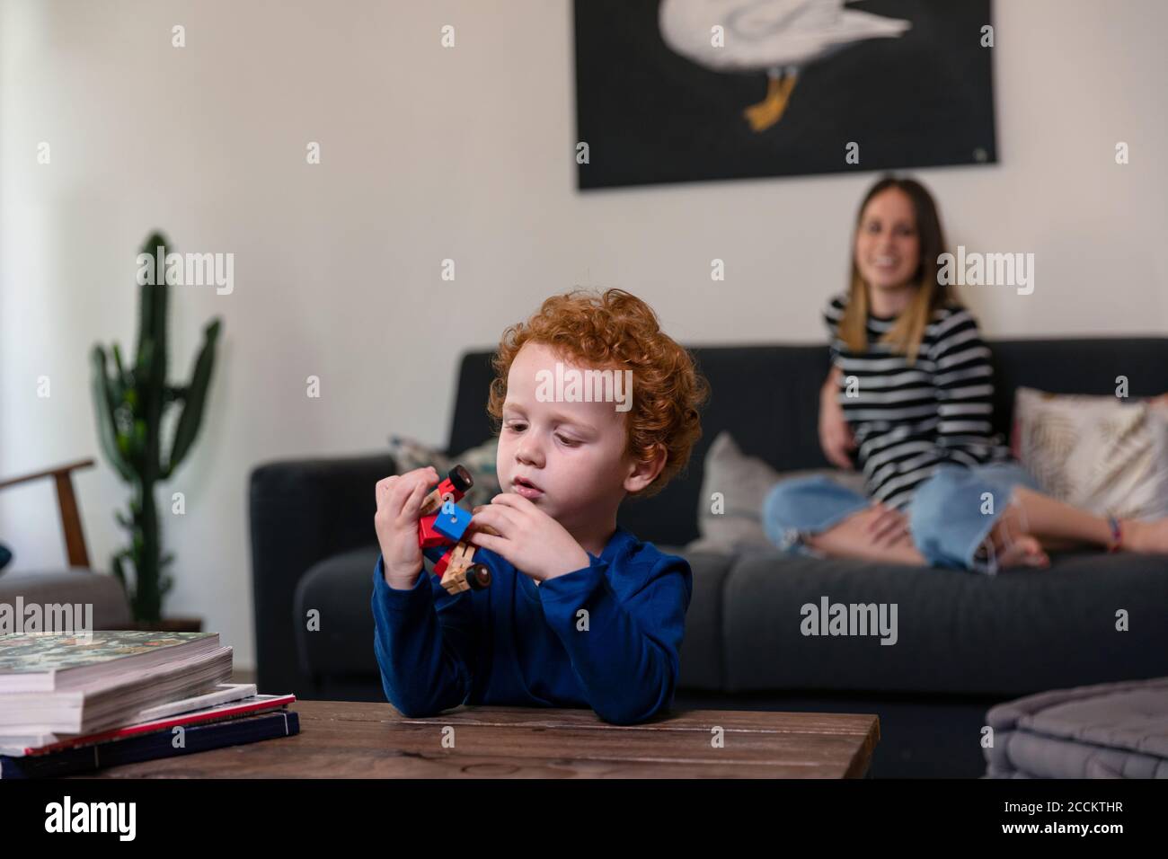 Mutter entspannt sich auf dem Sofa, während Sohn mit Spielzeug-Roboter spielt Auf dem Tisch zu Hause Stockfoto
