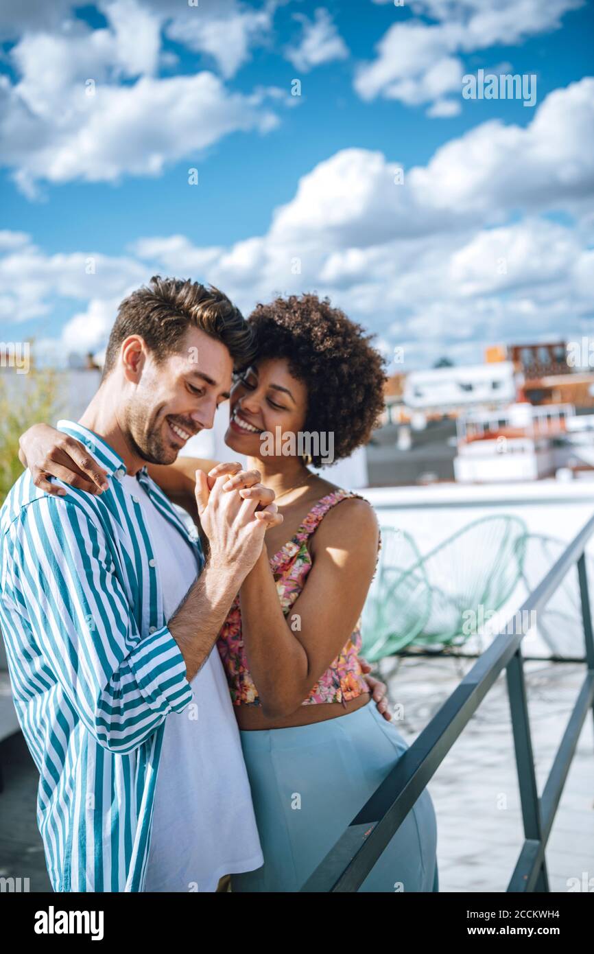 Fröhliches multiethnisches Paar, das auf der Penthouse-Terrasse tanzt Stockfoto