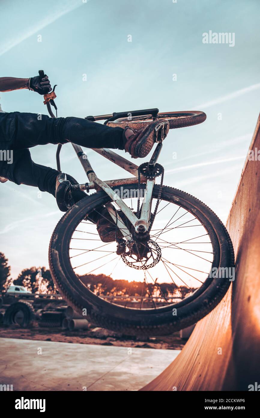 Junger Mann, der während des Sonnenuntergangs Fahrrad auf einer Rampe im Park reitet Stockfoto