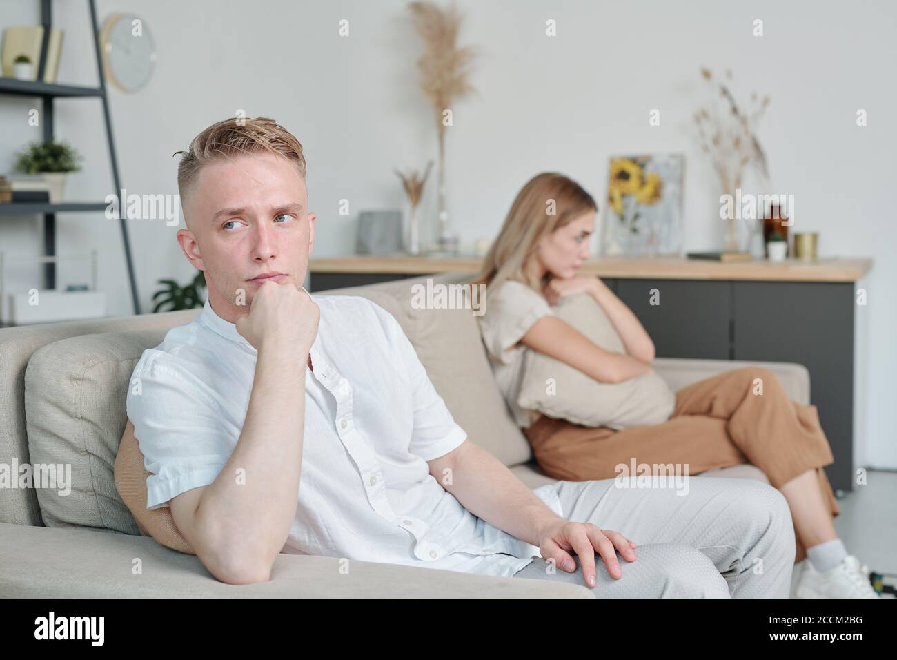 Junger beleidigter oder verärgerter Mann, der auf der Couch saß und dabei ignorierte Seine unglückliche Frau Stockfoto