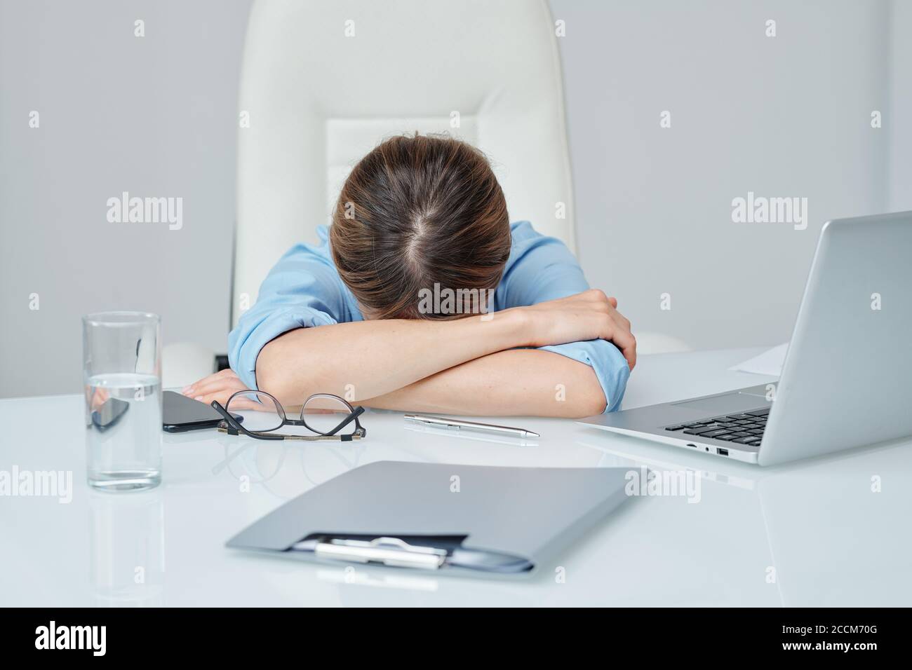 Junge erschöpfte Geschäftsfrau, die ihren Kopf auf gekreuzten Armen hält Schreibtisch Stockfoto