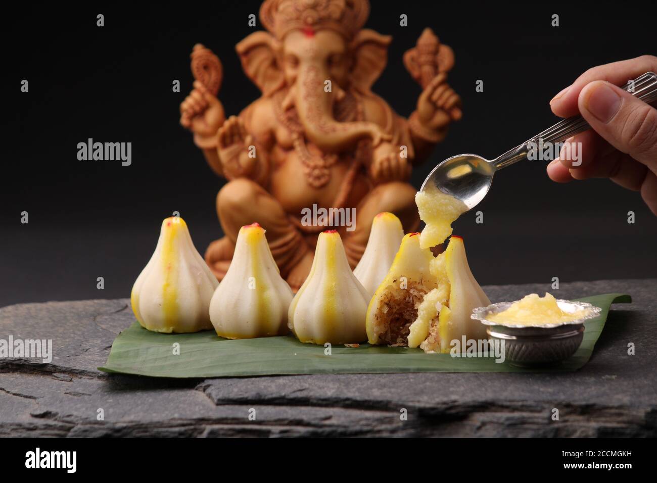 Modak- ein traditionelles Gericht auf Ganpati Festival in Indien. Serviert mit klarer Butter. Ganesh Idol im Hintergrund Stockfoto