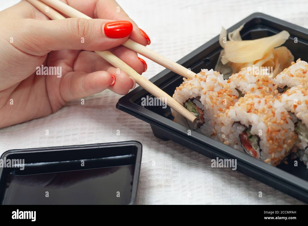 Frau essen zu Hause Sushi aus einem Behälter mit japanischen Sticks geliefert. Selektiver Fokus. Stockfoto