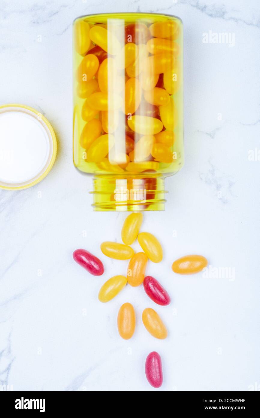 Vitamine. Bunte (rote und orange) Pillen (Dragee) in einer gelben Flasche auf einem Marmortisch. Das Konzept der Gesundheit. Selektiver Fokus, Draufsicht und Kopie Stockfoto