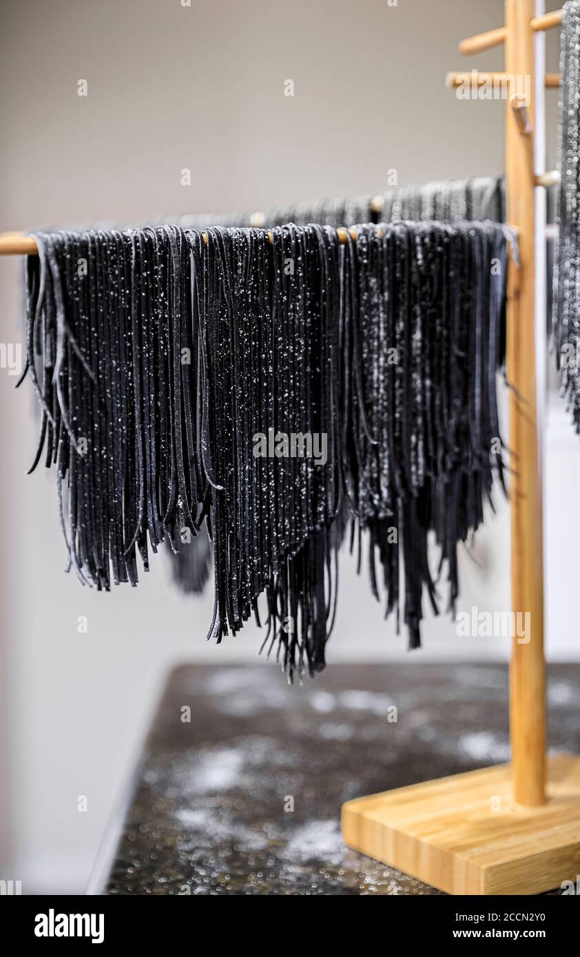 Frische Tintenfisch Tinte hausgemachte Spaghetti Pasta, bestreut mit Grießmehl hängen auf einem hölzernen Trockengestell Stockfoto