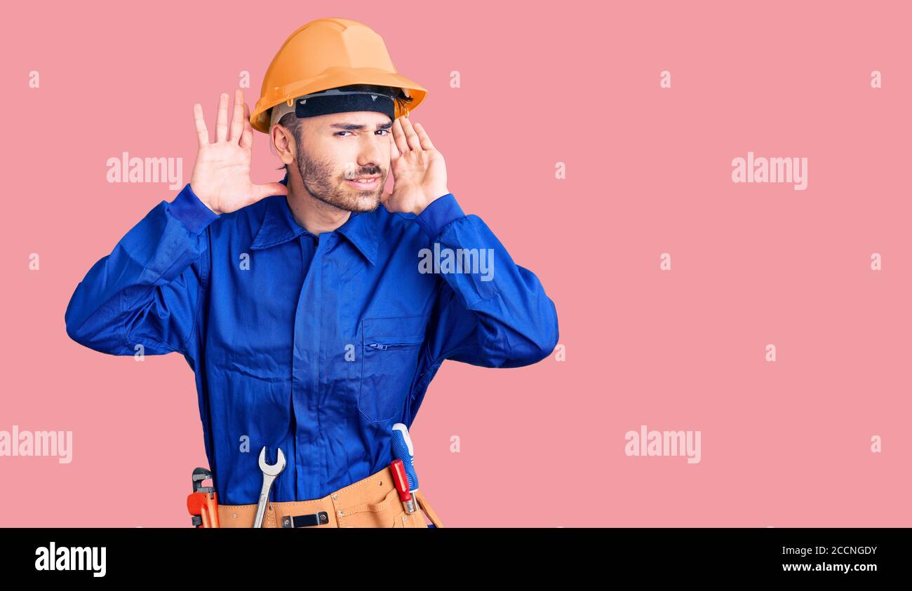 Junge hispanic Mann trägt Arbeiteruniform versucht, beide Hände auf Ohr Geste hören, neugierig auf Klatsch. Hörproblem, taub Stockfoto