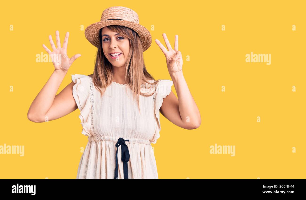 Junge schöne Frau trägt Sommerhut und T-Shirt zeigt und zeigt mit den Fingern Nummer acht, während lächelnd zuversichtlich und glücklich. Stockfoto