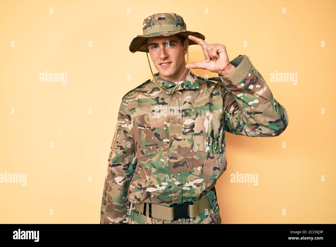 Junger schöner Mann trägt Tarnung Armee Uniform lächelnd und zuversichtlich Gestikulieren mit der Hand tun kleine Größe Zeichen mit Fingern suchen Und die Kamera Stockfoto