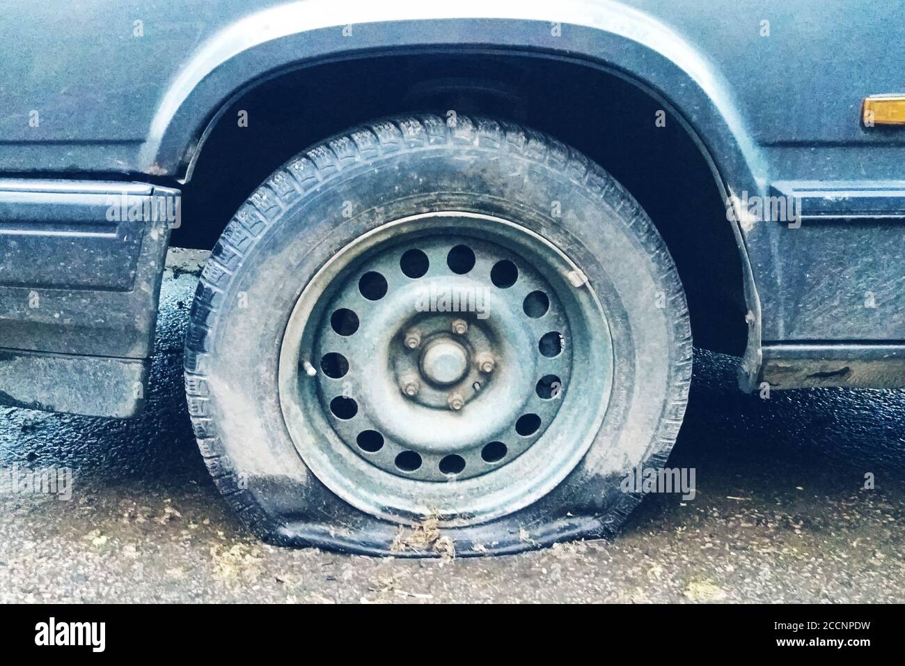 Reifenpanne des alten Autos im Freien, verschmutzter eingestürzter Reifen aus nächster Nähe Stockfoto