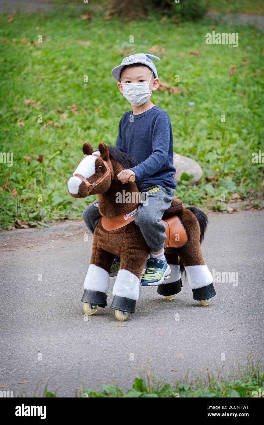 Ein junger asiatischer amerikanischer Junge reitet einen PONYCYCLE, ein Fahrrad für Kinder, das galoppiert & reitet wie ein Pony. In einem Park in Flushing, Queens, New York City. Stockfoto