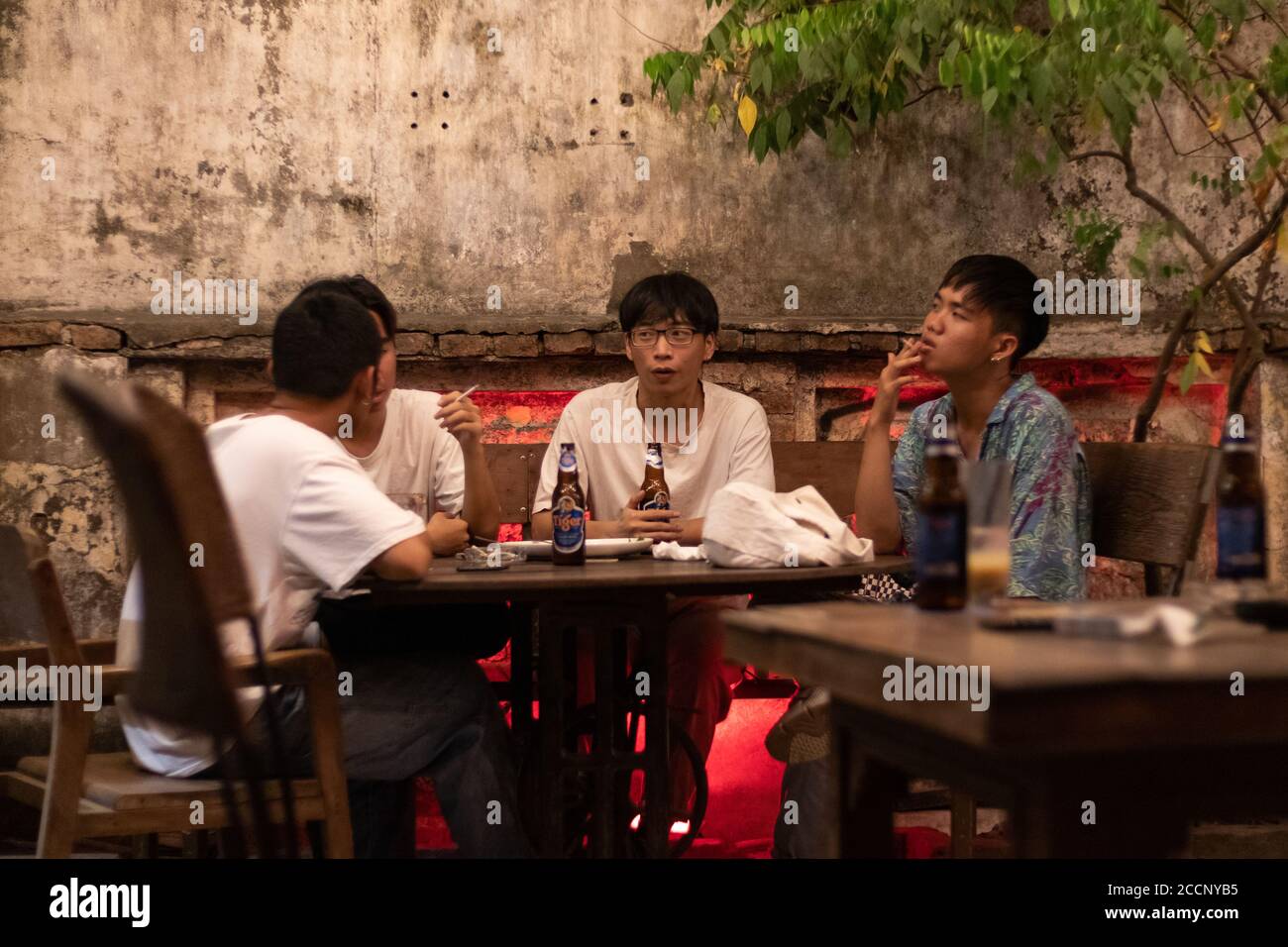 Gruppe von drei jungen Freunden, die Tiger Bier rauchen und trinken. Bar mit Vintage-Hipster-Atmosphäre. Vor Covid-19. Ho Chi Minh, Saigon, Vietnam Stockfoto