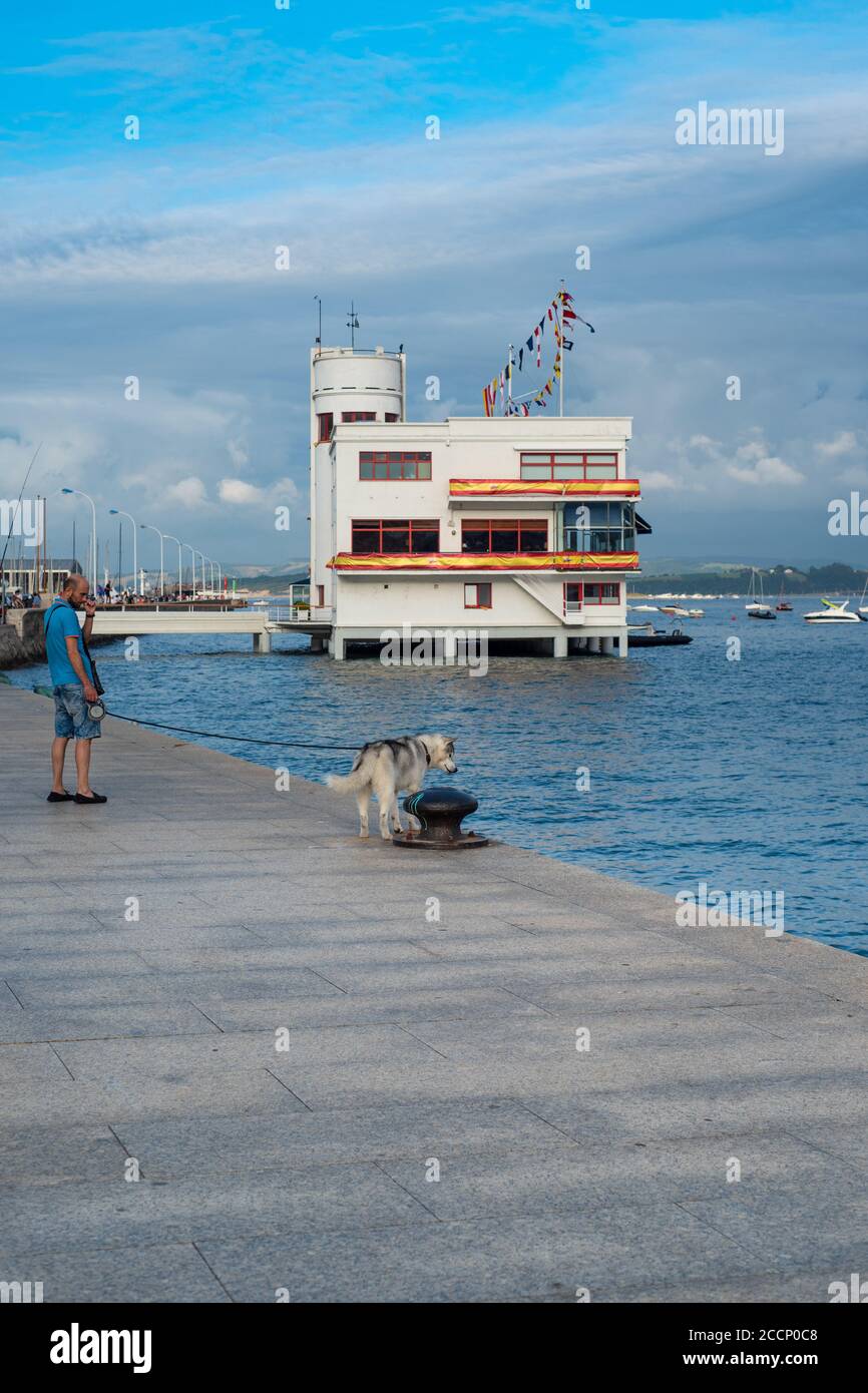 Kühner junger Mann bei einem sibirischen Husky in der Bucht von Santander, Spanien. Siberian Husky Blick auf das Meer in Puerto Chico, Santander, Kantabrien. Stockfoto