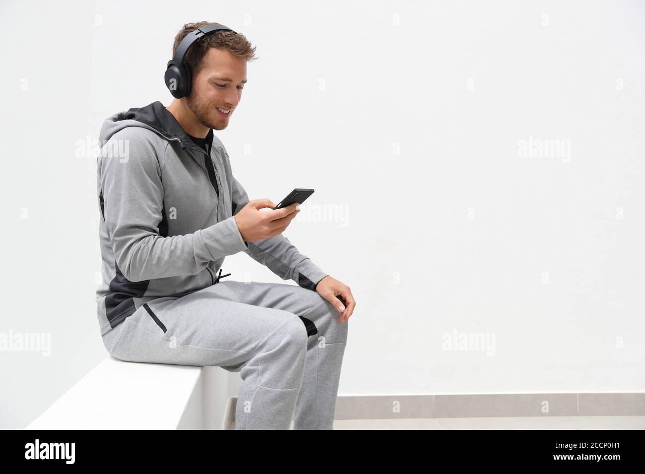 Mann hört Musik Handy-App trägt Kopfhörer sitzen zu Hause. Gesunder Lifestyle-Sportler mit Smartphone auf Jogging-Pause im Freien Stockfoto