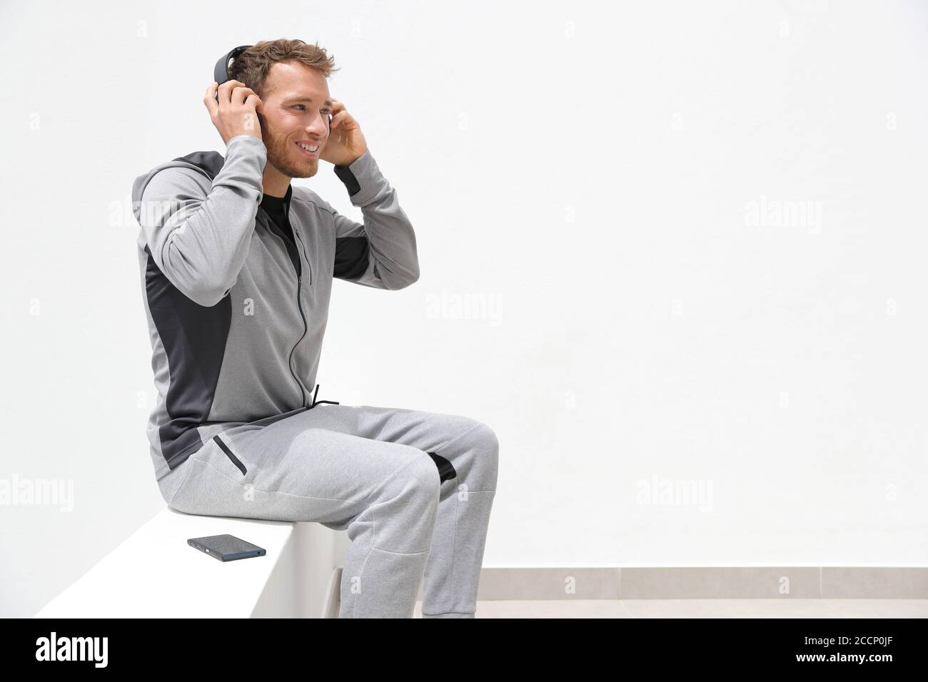 Mann hört Musik Handy-App trägt Kopfhörer sitzen zu Hause. Gesunder Lifestyle-Sportler mit Smartphone auf Jogging Pause im Freien Stockfoto