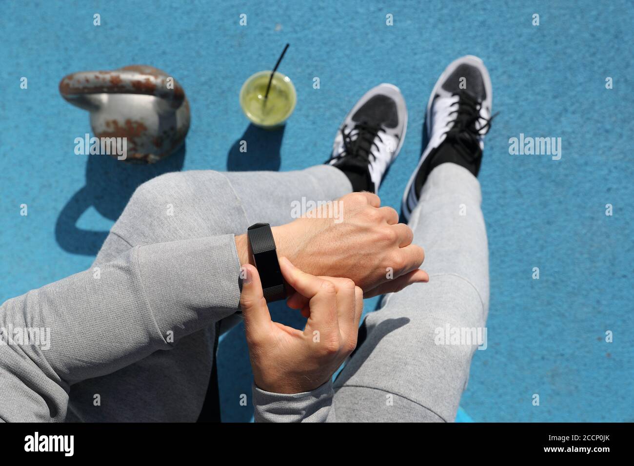 Gym Mann berührt Smartwatch Bildschirm während des Trainings Krafttraining. Draufsicht von oben: kettlebell Gewichte, grüner Smoothie, Körper und Beine. POV Stockfoto