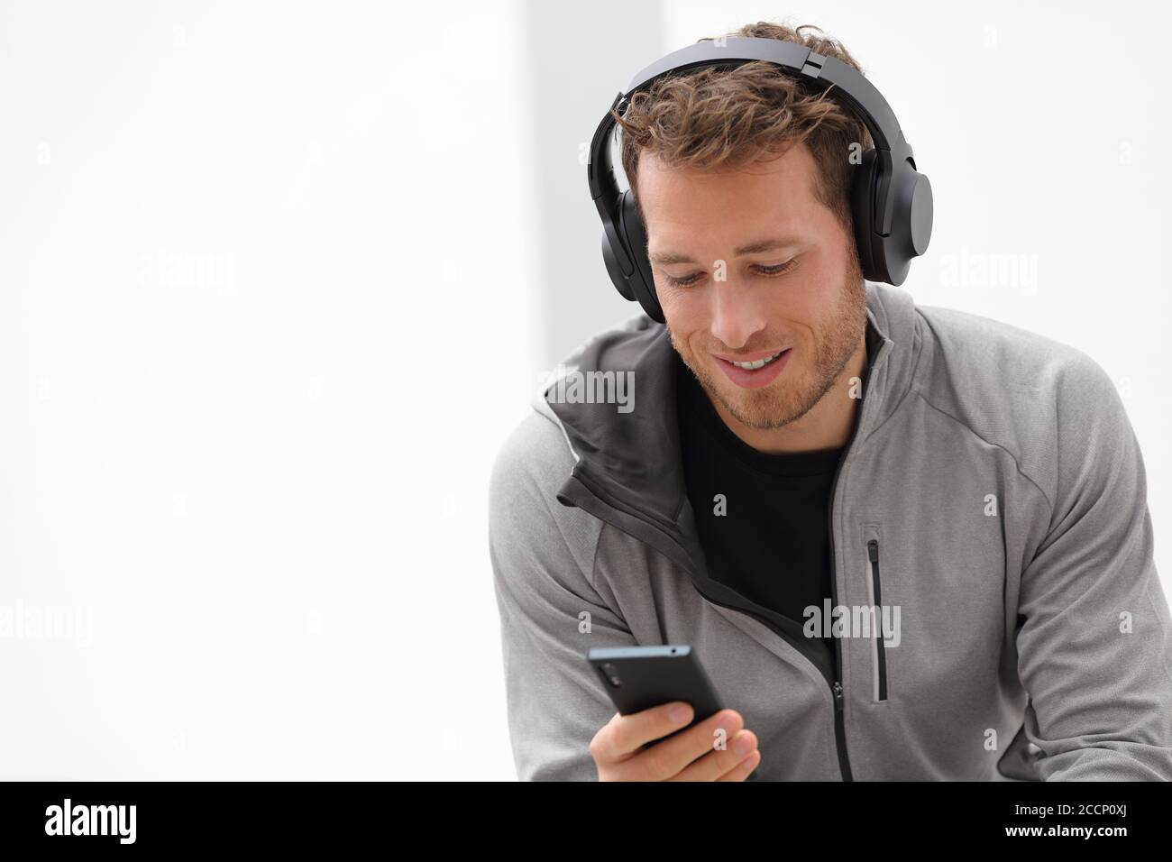 Mann hört Musik Handy-App tragen Headset zu Hause sitzen. Gesunder Lifestyle-Sportler mit Smartphone auf Jogging-Pause im Freien Stockfoto