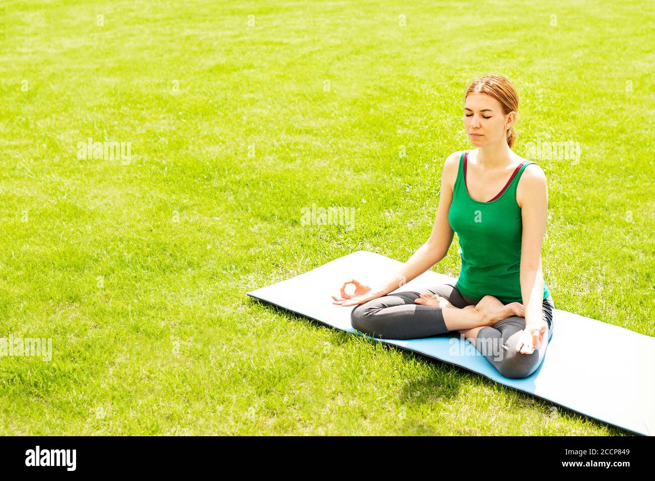 Eine Frau praktiziert Yoga im Freien auf dem Gras. Speicherplatz kopieren Stockfoto