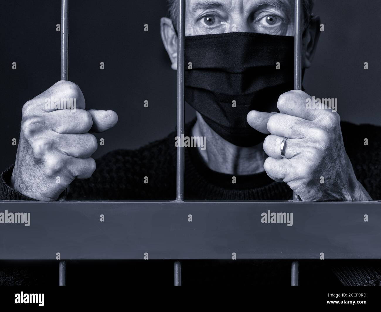 Ein Mann, der eine schwarze Maske trägt, klemmt die Gitter eines Sicherheitstors während der Sperre wegen der Covid-19 Corona Virus Pandemie. Stockfoto
