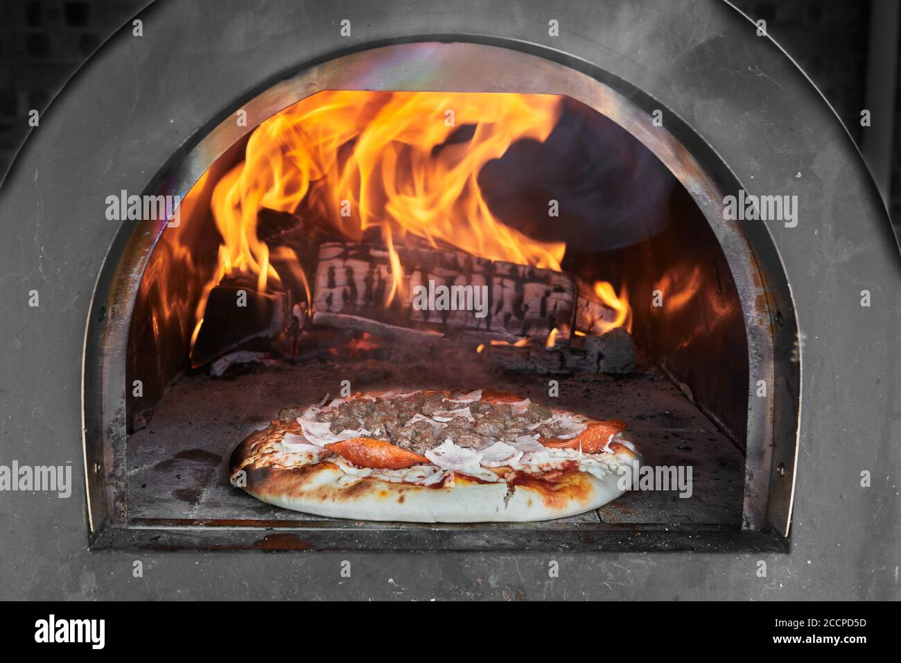 Vorzeitig gekochte Pizza vor flammendem Holz in einem Pizzaofen. Stockfoto