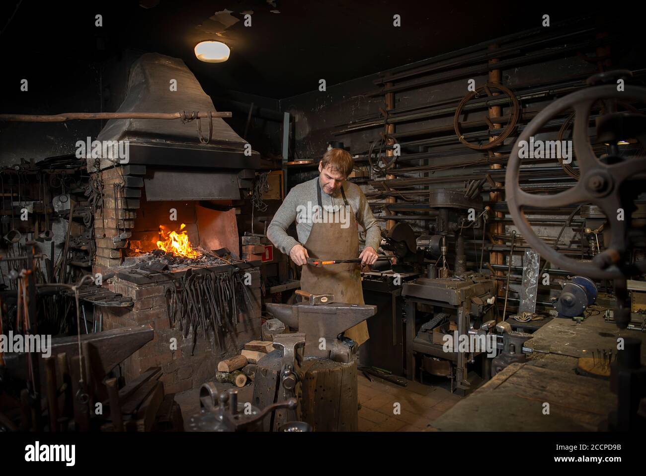 Der Schmied schmiedet das rotglühende Metall manuell auf dem Amboss In Schmiede mit Funkenfeuerwerk Stockfoto