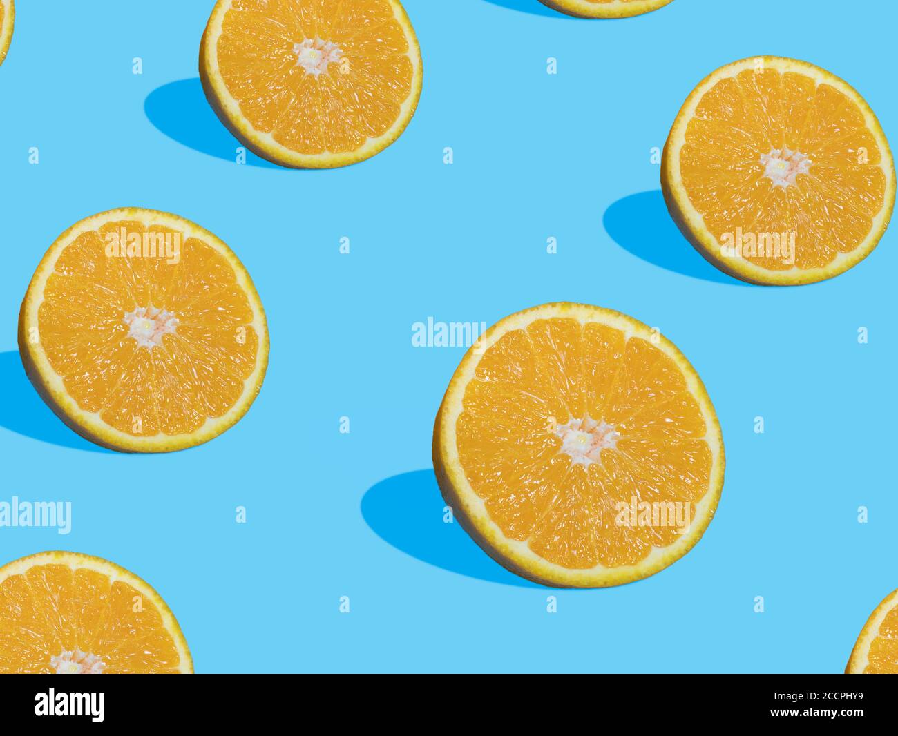 Frische orangene Scheiben auf blauem Hintergrund mit Schatten, Draufsicht, flaches Lay, Nahaufnahme, Muster. Sommer und gesunde Zitrusfrüchte Konzept Stockfoto