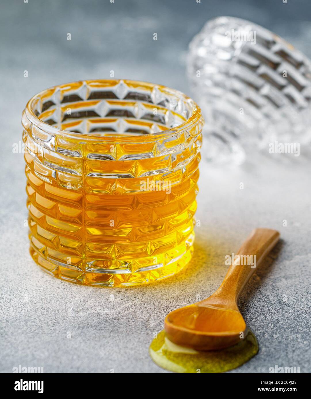 Flüssiger Blütenhonig in einem Glas mit Holzhonigtaube auf Beton- oder Steingrund. Selektiver Fokus Stockfoto