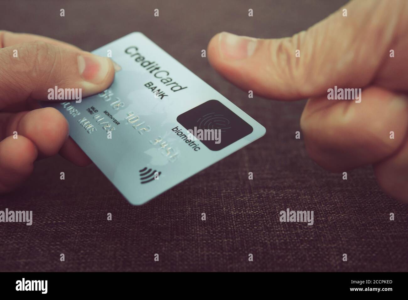 Nahaufnahme der männlichen Hände mit Kreditkarte mit Fingerabdruck-Scanner und Einbettung des Daumens, um online zu bezahlen. Konzept der Verwendung biometrischer Technologie in Stockfoto