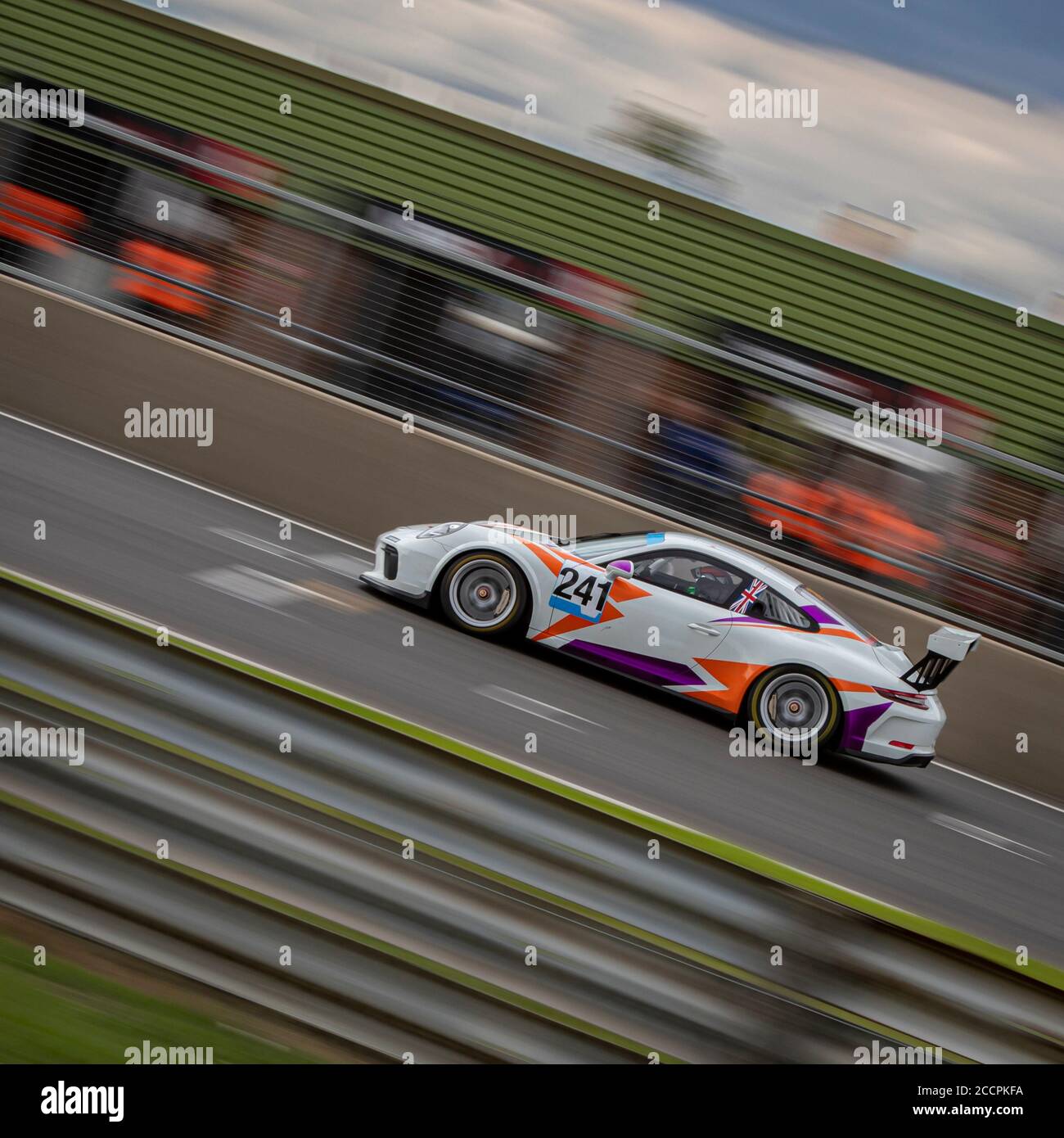 Eine Schwenkaufnahme eines weißen, violetten und orangen Rennwagens, der eine Rennstrecke fährt. Stockfoto